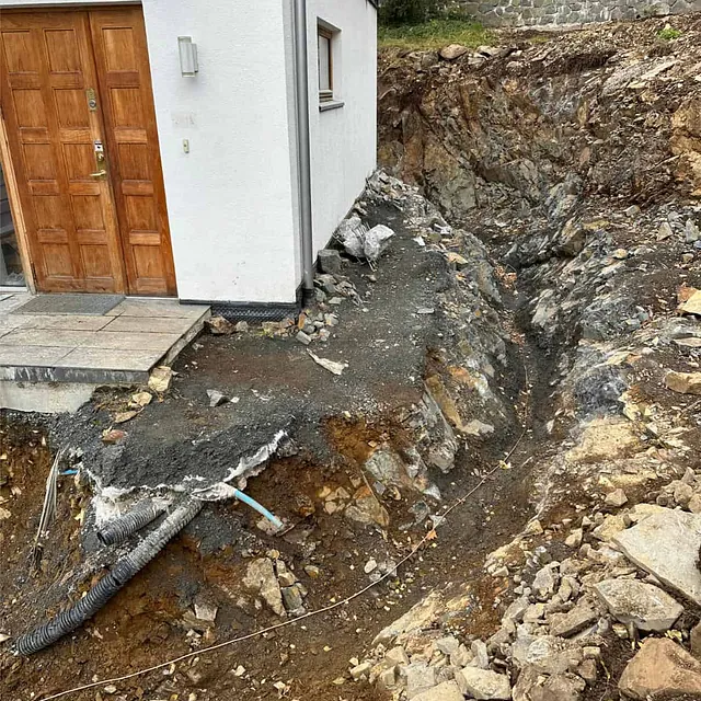 Berg skjæres ut langs grunnmur for å utvide terreng og klargjøre nytt uteområde.
