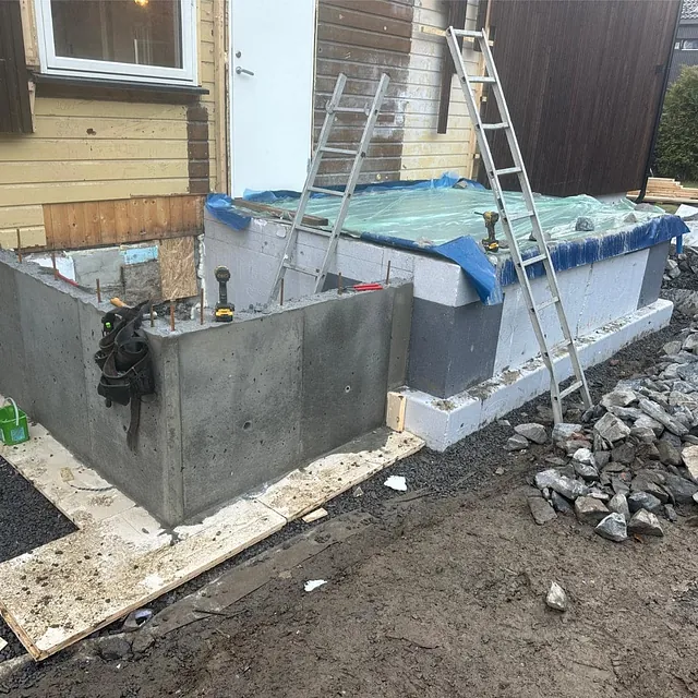 Nytt tilbyggsfundament med betongvegger og isolasjon under videre oppføring av bygget.