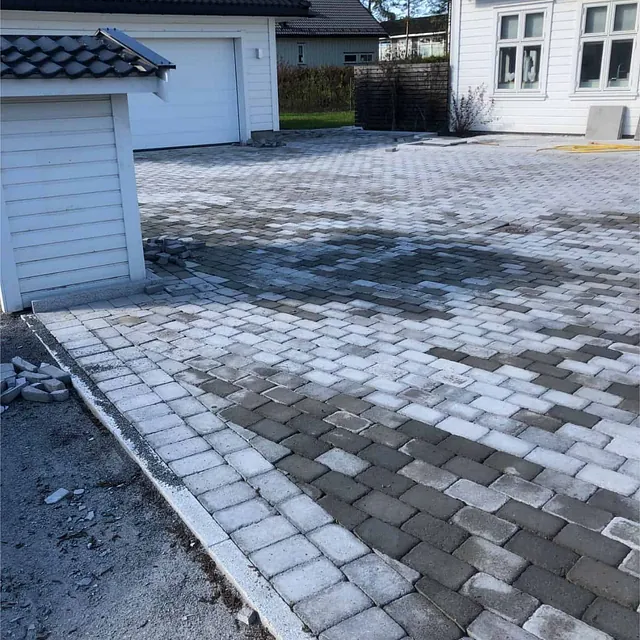 Stor gårdsplass med belegningsstein og kantstein gir ryddig adkomst til bolig og garasje.