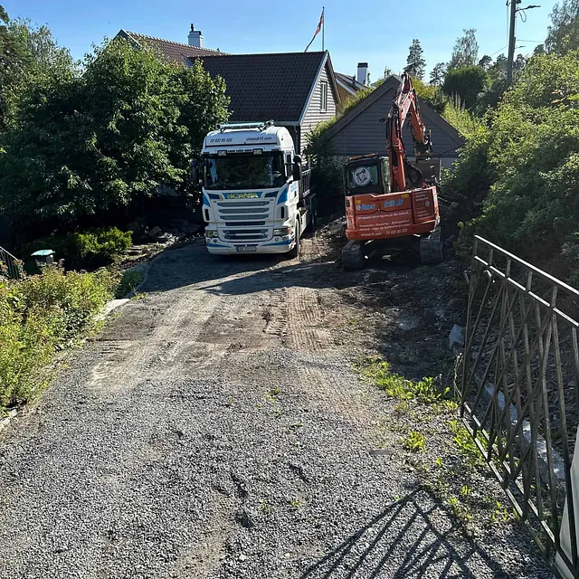 Gravemaskin og lastebil står på tomt under terrengarbeid og oppføring av støttemur.