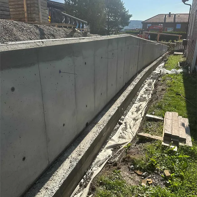 Ferdigstøpt betongmur langs tomtegrense som gir stabilitet og oppstøtting av terrenget.
