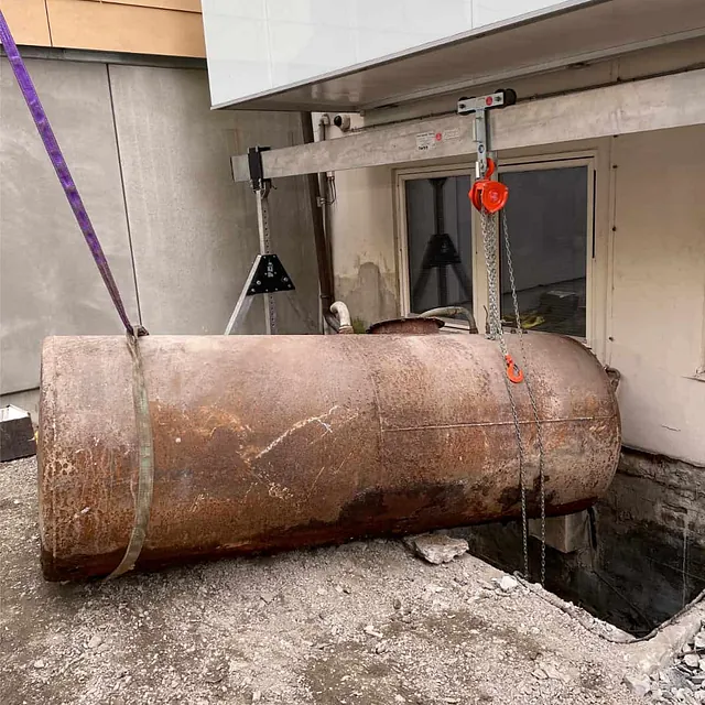 Gammel oljetank heises opp fra utgravd område for sanering ved bygning.