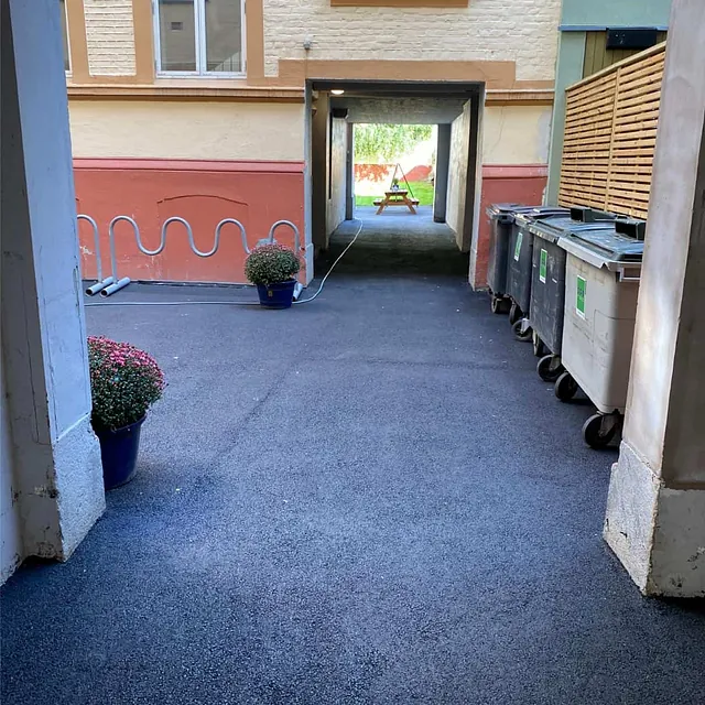 Ferdigstilt asfaltert gårdsrom med ny overflate og renovasjonsløsning ved bygården.