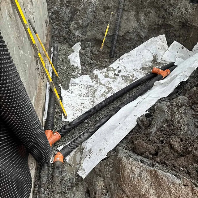 Drensrør og overvannsrør legges i pukk og fiberduk for sikker vannhåndtering.