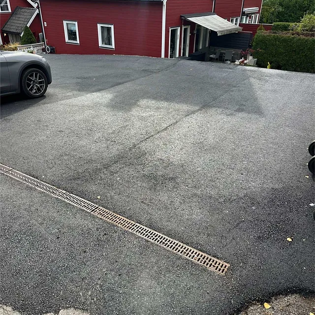 Nyasfaltert parkeringsplass med sluk for overvannshåndtering foran boligbebyggelse.