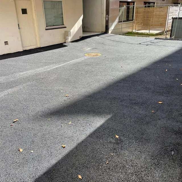 Ferdigstilt asfaltert gårdsplass med sluk og jevnt dekke ved leilighetsbygg.