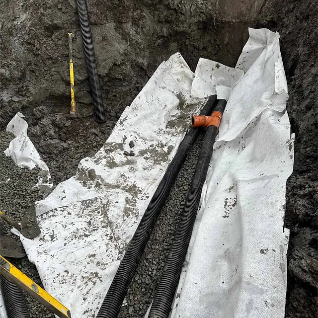 Drensrør plassert i fiberduk og pukk for effektiv bortledning av vann fra grunnmuren.