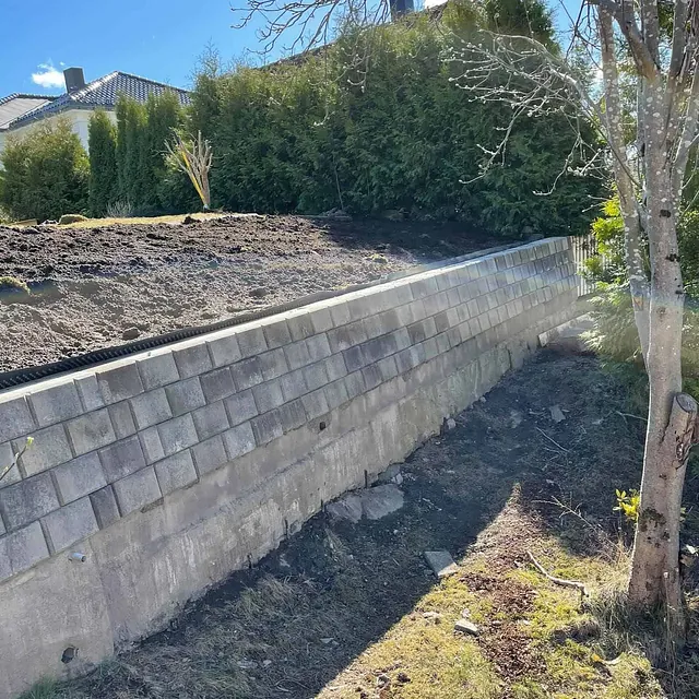 Støttemur av betong og murblokker sikrer terreng langs opparbeidet tomt ved bolig.