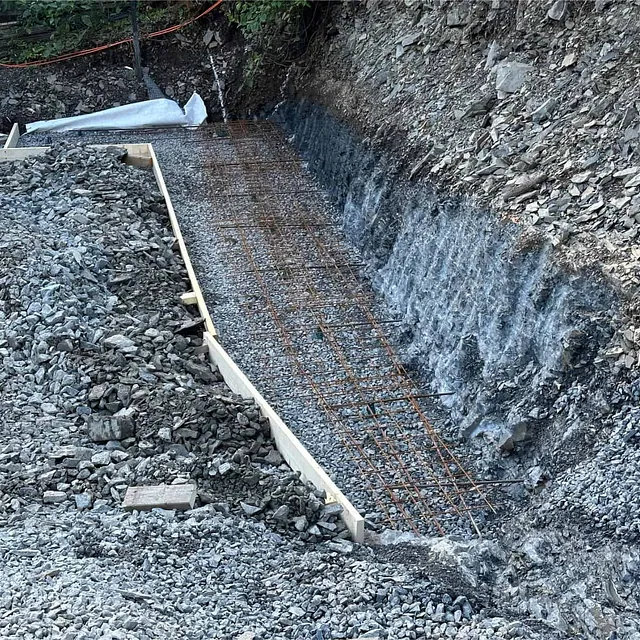 Armering og forskaling klargjøres for fundament langs fjellskjæring på byggeplass.