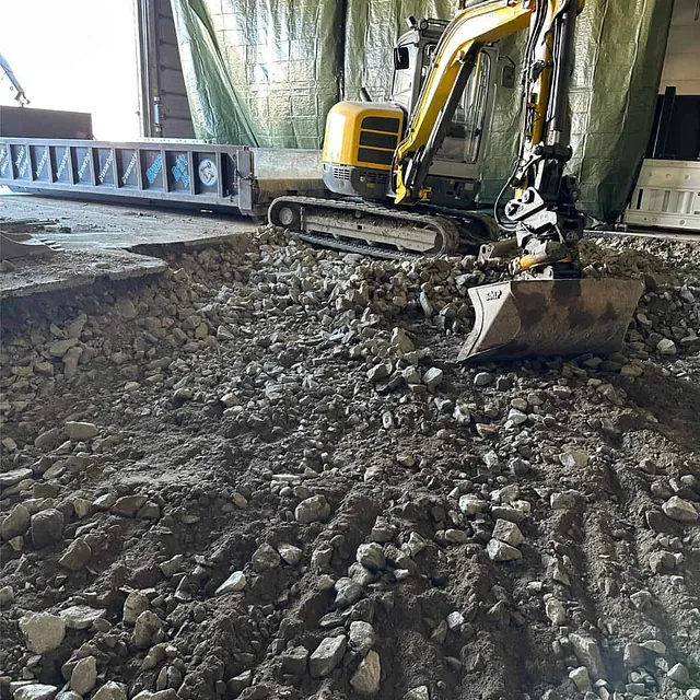 Minigraver fordeler og avretter masser som forberedelse til nytt isolert betonggulv.
