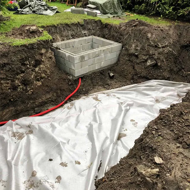 Utgravd område med teknisk rom og fiberduk klargjort for basseng- og terrasseanlegg.