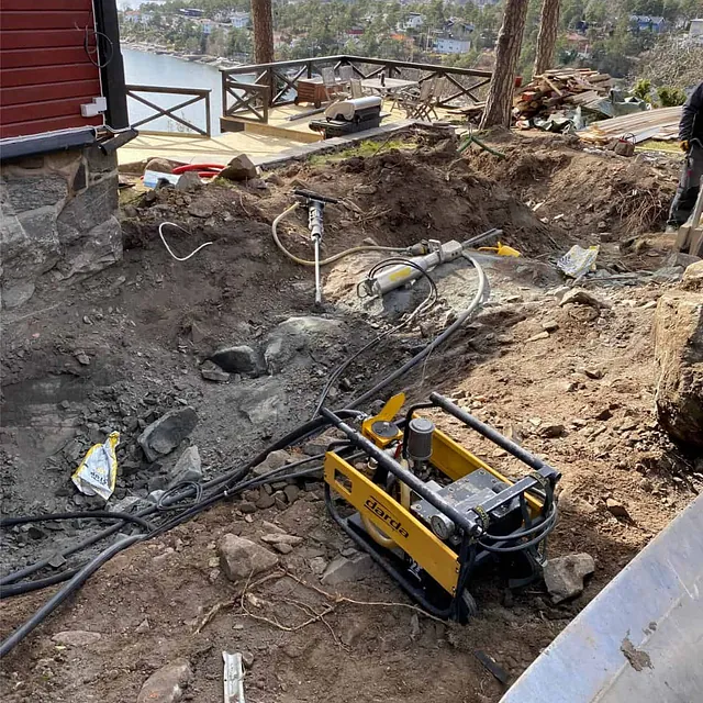 Bergarbeider pågår ved bolig med hydraulisk splitteutstyr før utgraving og terrengforming.