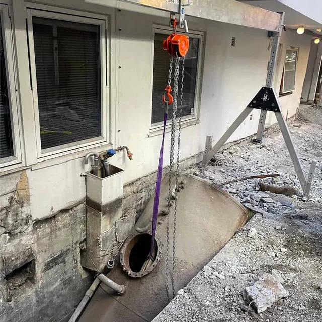 Oljetank heises opp fra utgravd område under sanering og fjerning ved boligblokk.