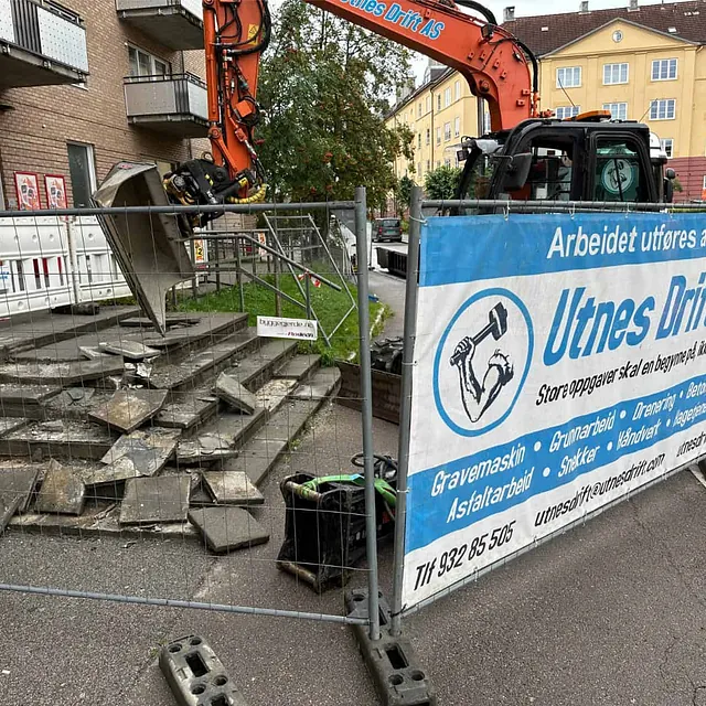 Eksisterende trapp rives med gravemaskin som første steg i rehabilitering av inngangspartiet.