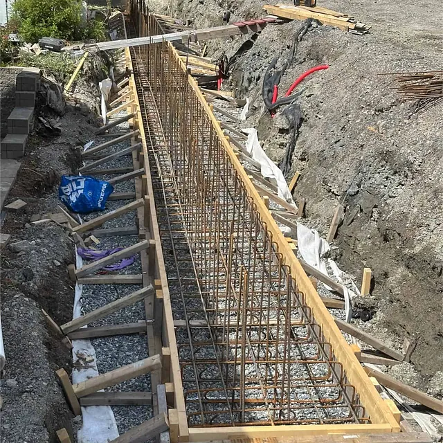 Armeringsjern og forskaling klargjort for støping av lang støttemur langs tomtegrensen.