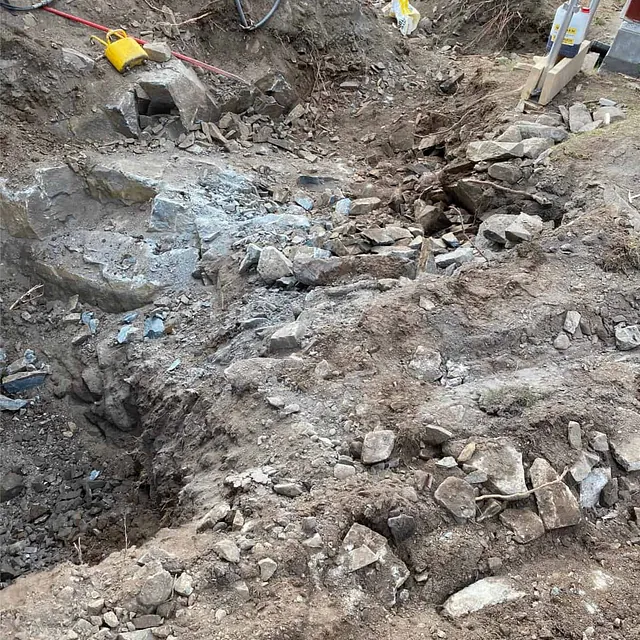 Oppsprukket berg fjernes etter kiling og boring som del av pågående grunnarbeider.