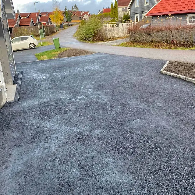 Nyasfaltert innkjørsel ved boligområde, omgitt av bolighus, hekker og stille nabolag.