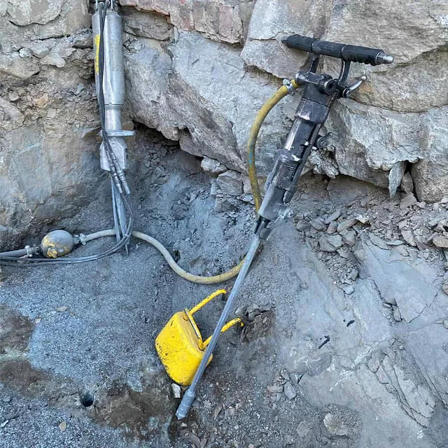 Hydraulisk bore- og kileutstyr brukes for kontrollert splitting av berg tett inntil bygning.
