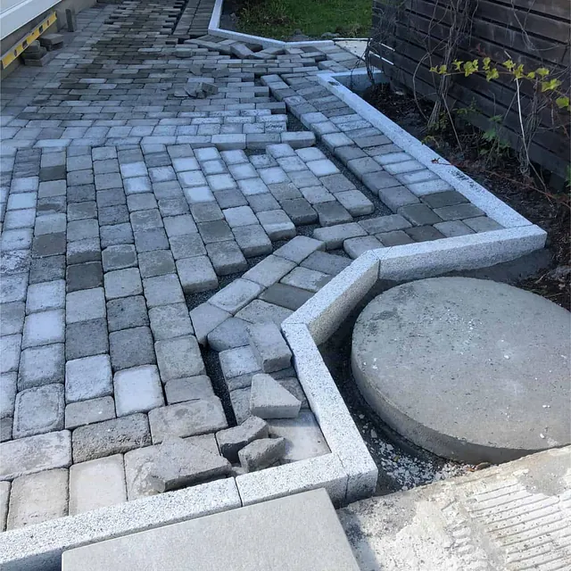 Gangareal med belegningsstein formes rundt kummelokk og kantstein ved bolig og hage.