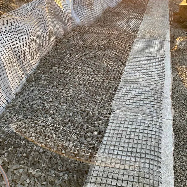 Steinfylling og geonett legges bak natursteinsmur for stabilisering og terrengsikring.