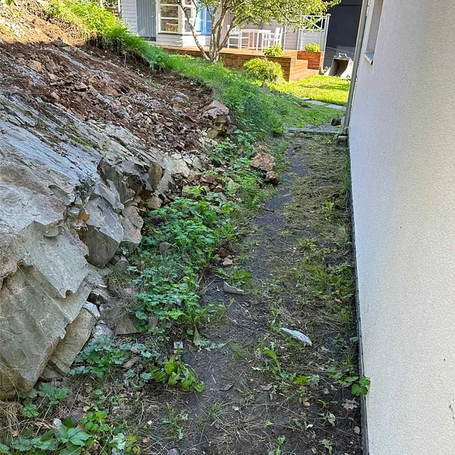 Eksisterende bergskråning og terreng langs bolig før oppstart av sprenging og grunnarbeider.