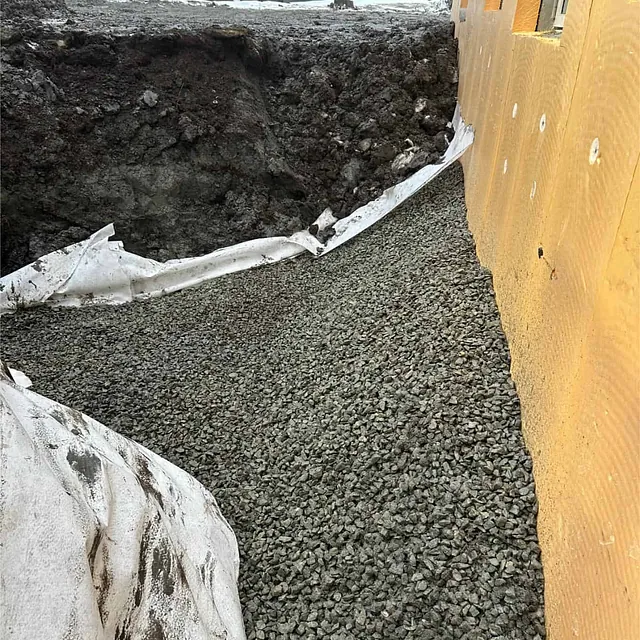 Pukk og fiberduk etablert langs isolert grunnmur for varig drenering og fuktsikring.