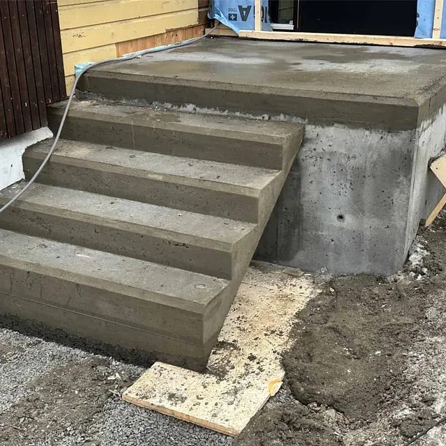 Ferdigstøpt betongtrapp og platting ved inngangsparti som del av nytt tilbygg.