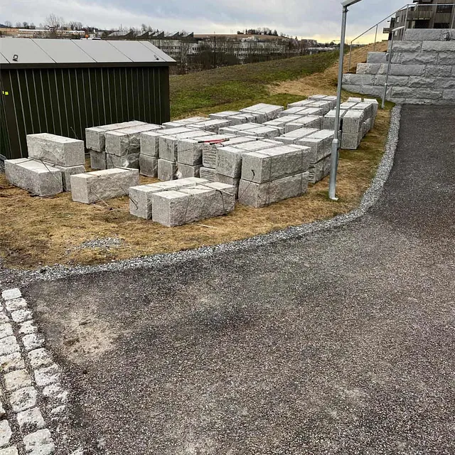 Natursteinsblokker lagret på anleggsområdet før oppstart av murarbeid og terrengsikring.