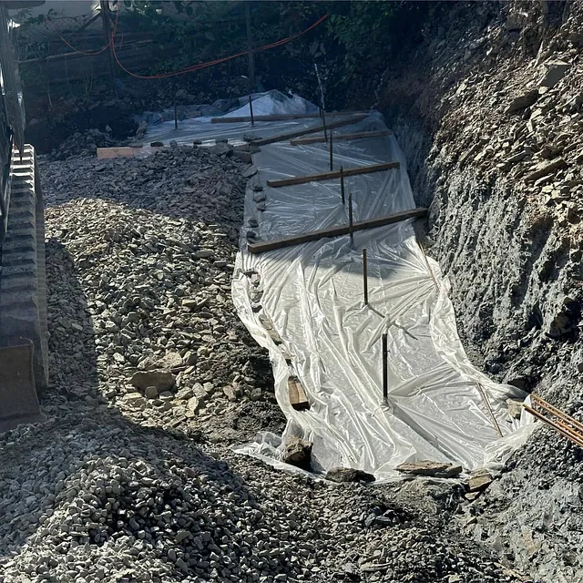Plastdekke og pukk klargjør fundament langs fjellskråning før armering og støping.