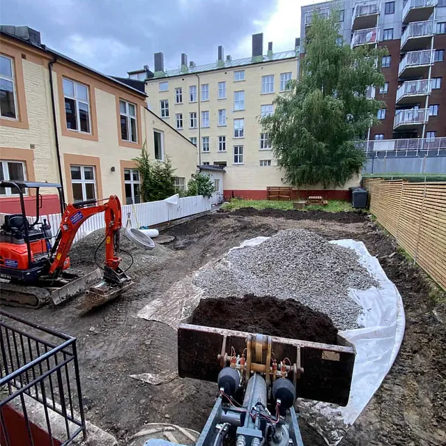 Grunnarbeider i bakgård med gravemaskin, pukk og klargjøring for nytt uteanlegg.