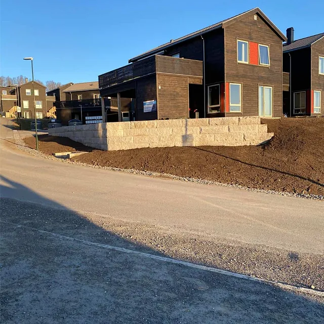 Ferdigstilt natursteinsmur langs boligområde med opparbeidet terreng og sikret skråning.