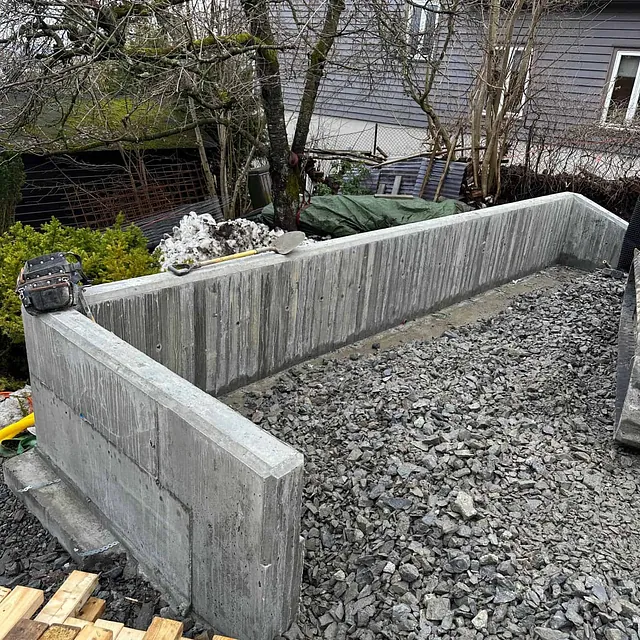 Ferdigstøpte betongmurer omslutter oppfylt område med pukk, klart for videre bygging.