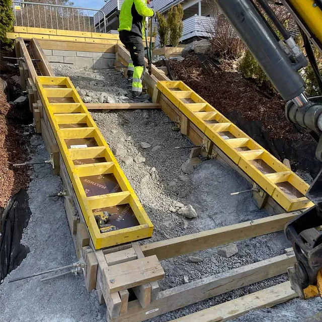 Forskalingsarbeid pågår for støping av ny betongtrapp i skrånende terreng ved bolig.