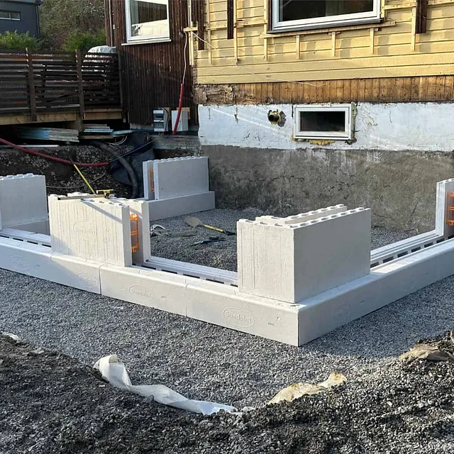 Første rad med forskalingsblokker montert på avrettet pukk som fundament for tilbygg.