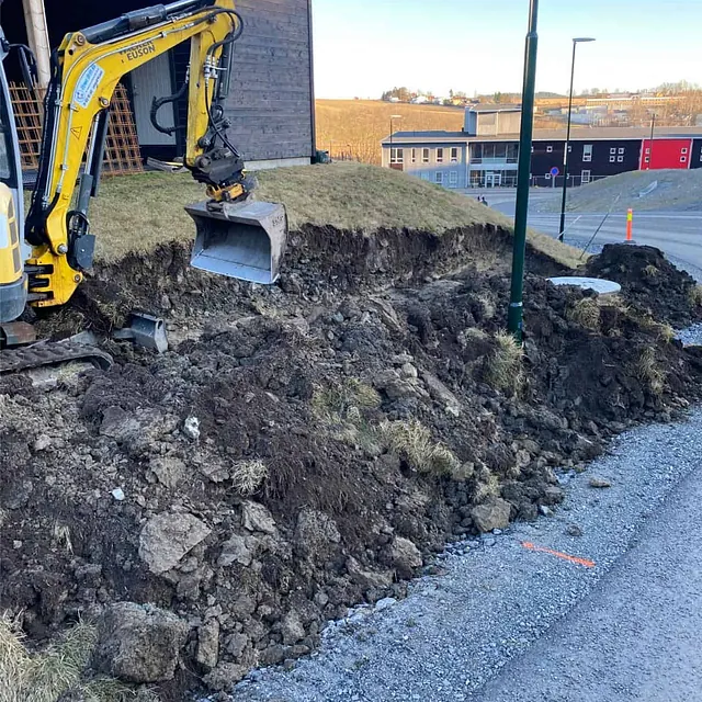 Utgraving langs skråning med gravemaskin som forberedelse til etablering av ny støttemur.